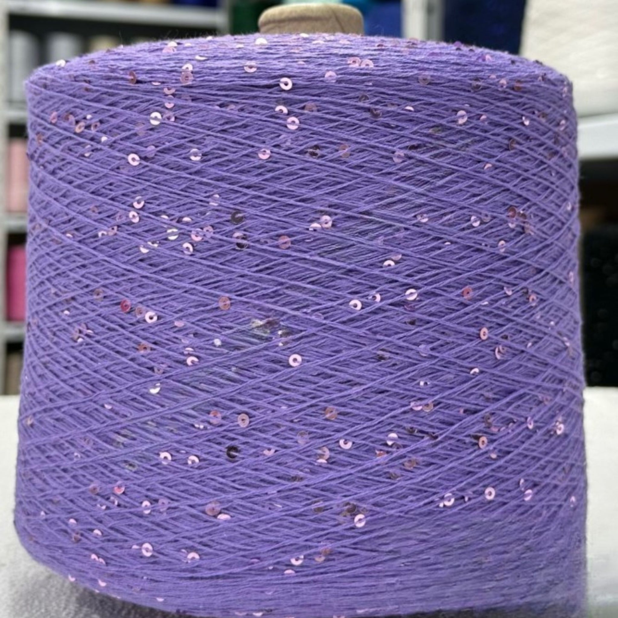 Spool of purple yarn with sequins on a white background
