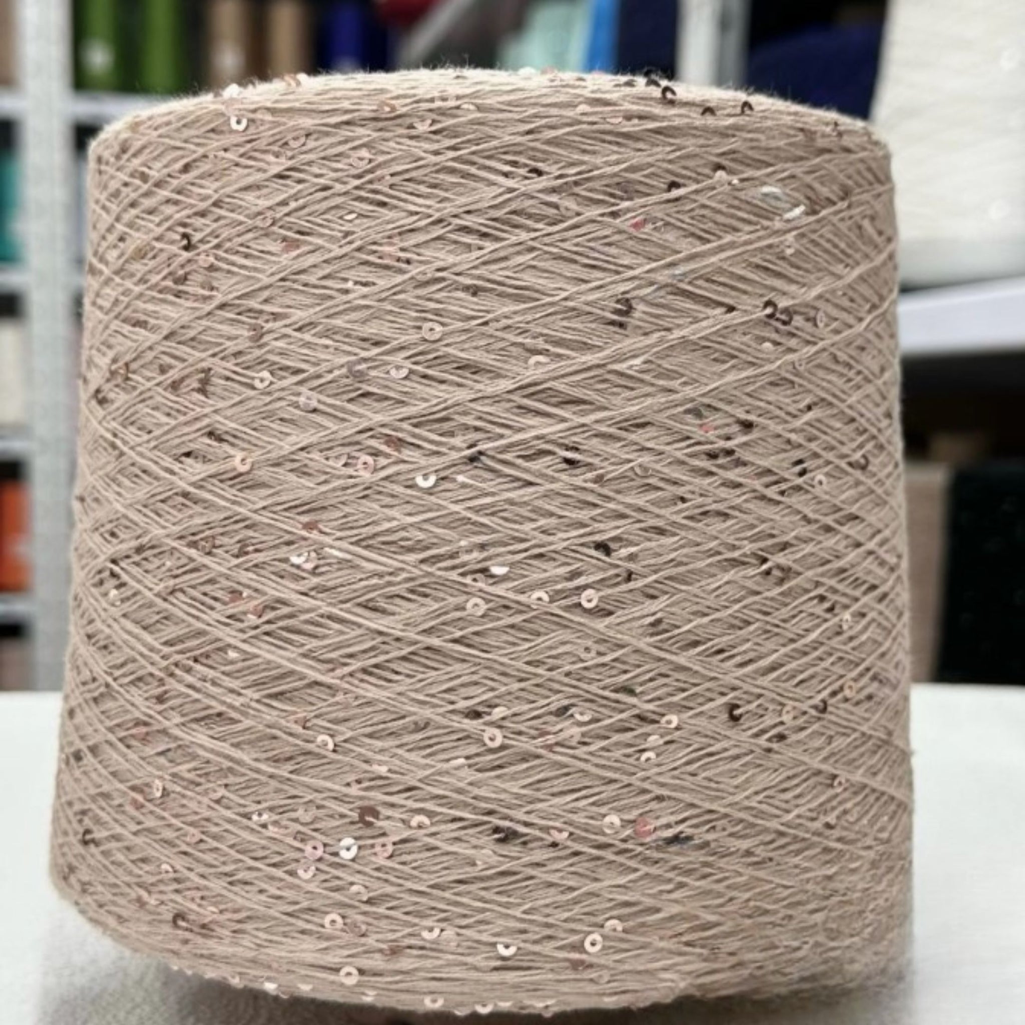 Spool of beige yarn with sequins on a blurred background
