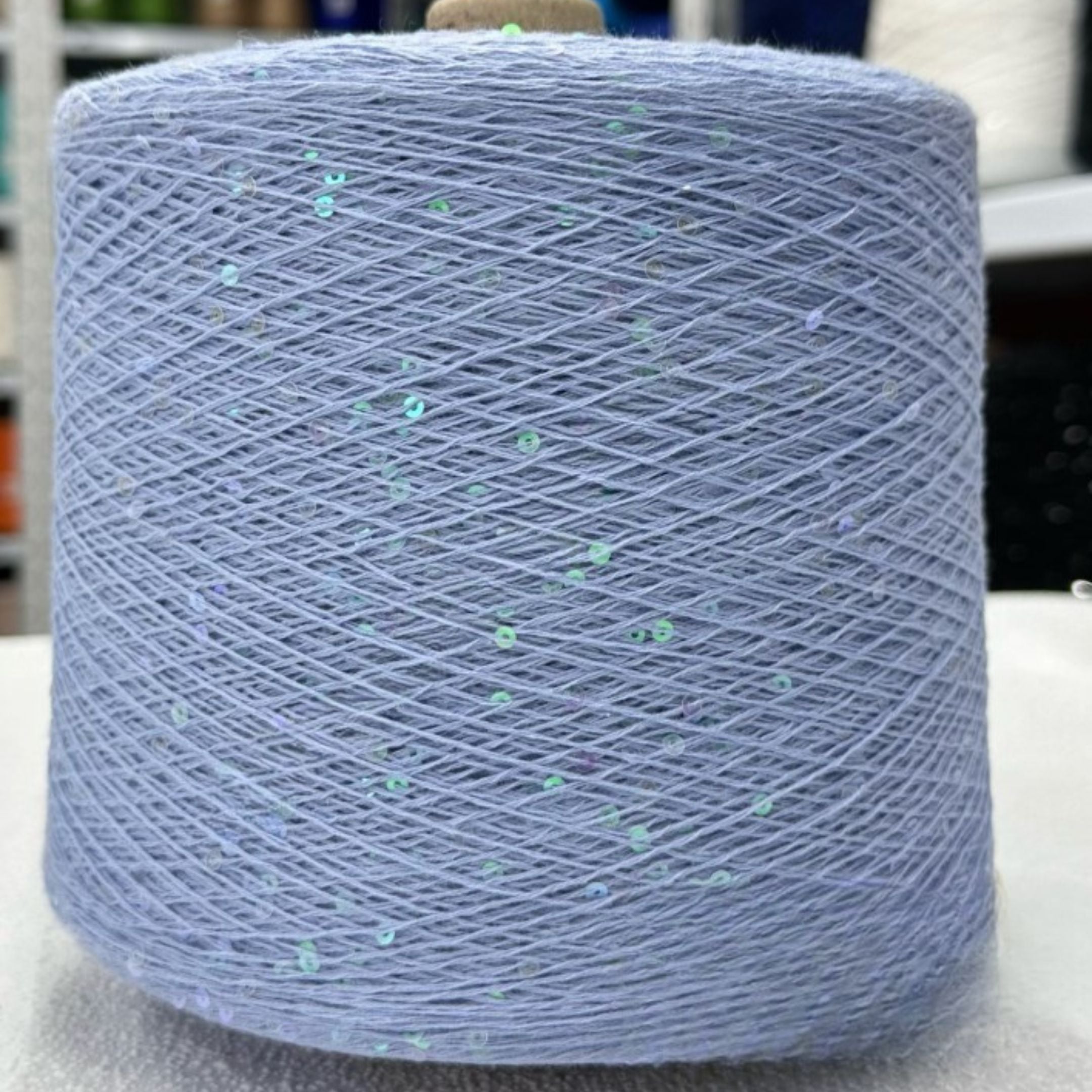 Spool of blue yarn with glittery specks on a white surface