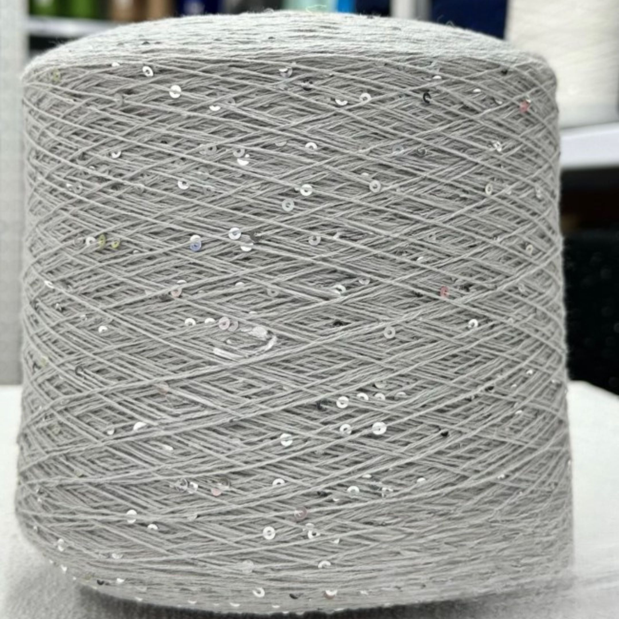 Spool of gray yarn with embedded sequins on a white surface