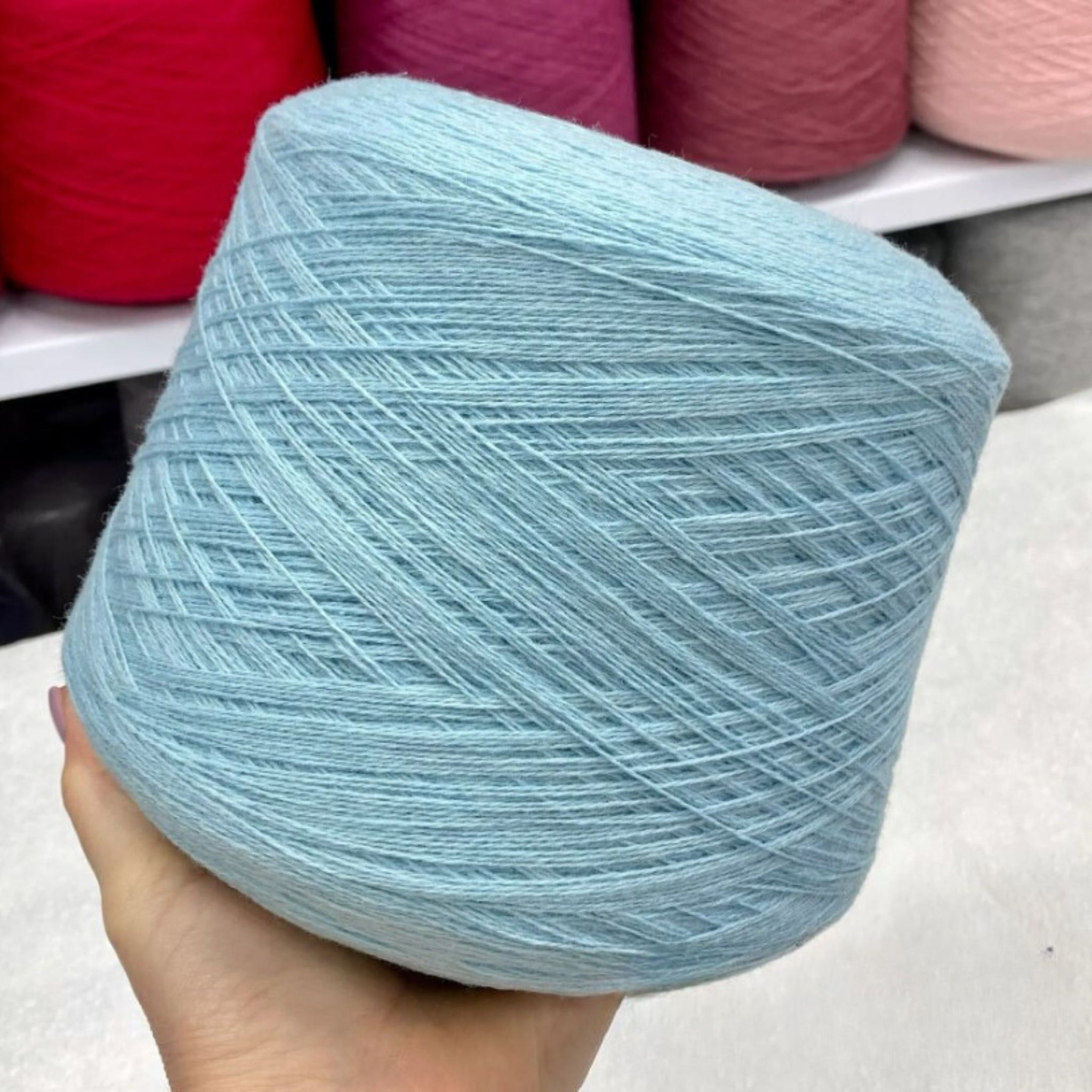 Light blue merino yarn ball held in a hand with more yarn balls in the background.