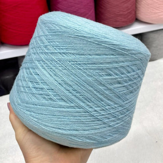 Light blue merino yarn ball held in a hand with more yarn balls in the background.