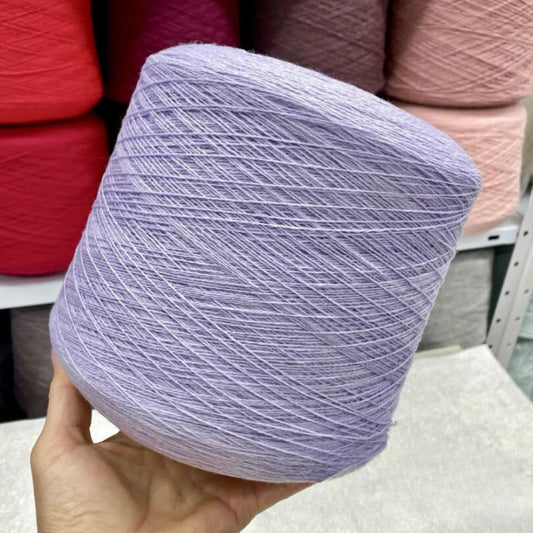 Hand holding a ball of light purple merino yarn with other yarn balls in the background.