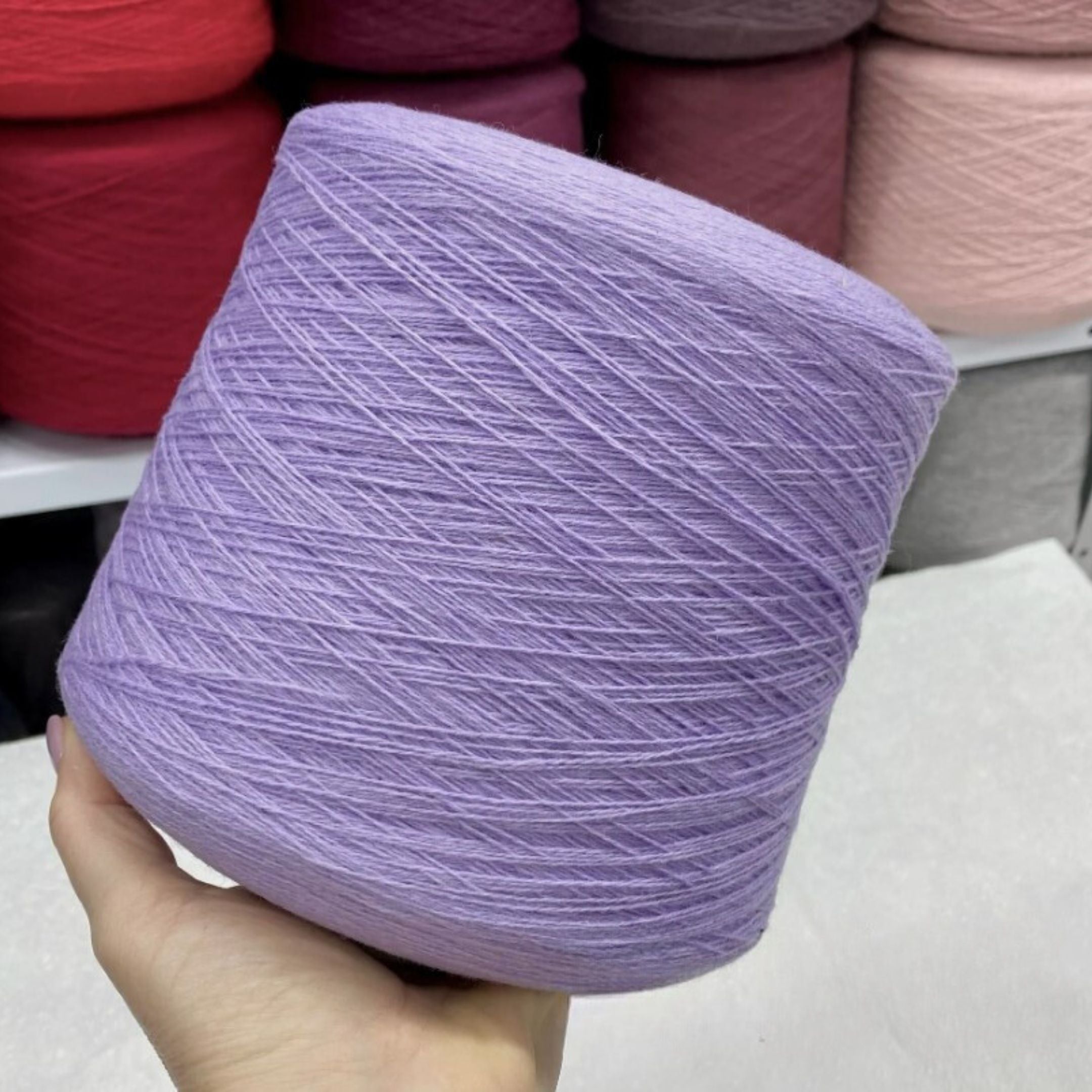 Hand holding a purple skein of merino yarn with other yarn colors in the background