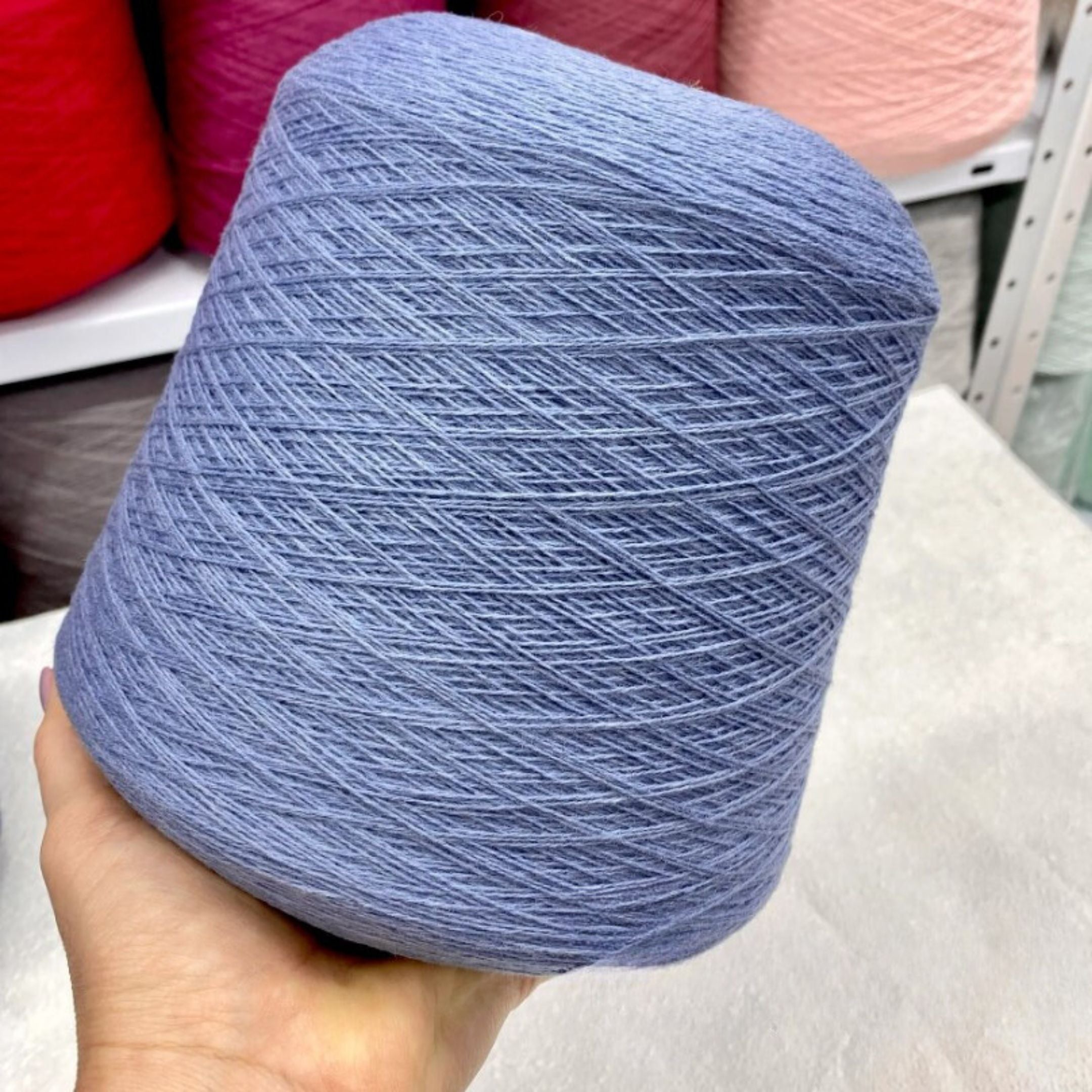 Hand holding a blue m skein of  merino yarn with pink yarn in the backgroundr