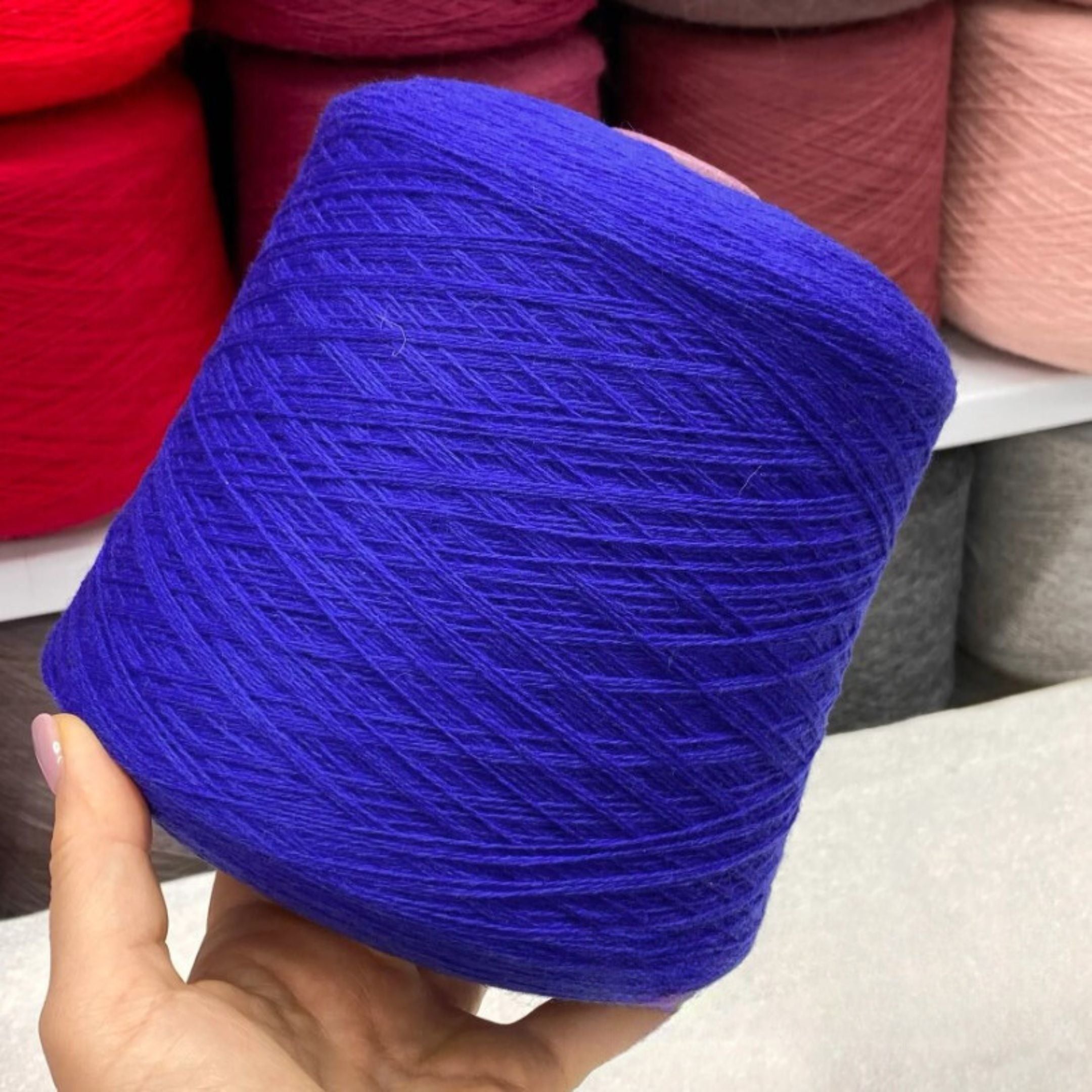 Blue merino yarn ball held by a hand with colorful yarn balls in the background