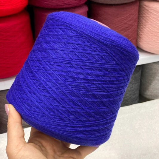 Blue merino yarn ball held by a hand with colorful yarn balls in the background