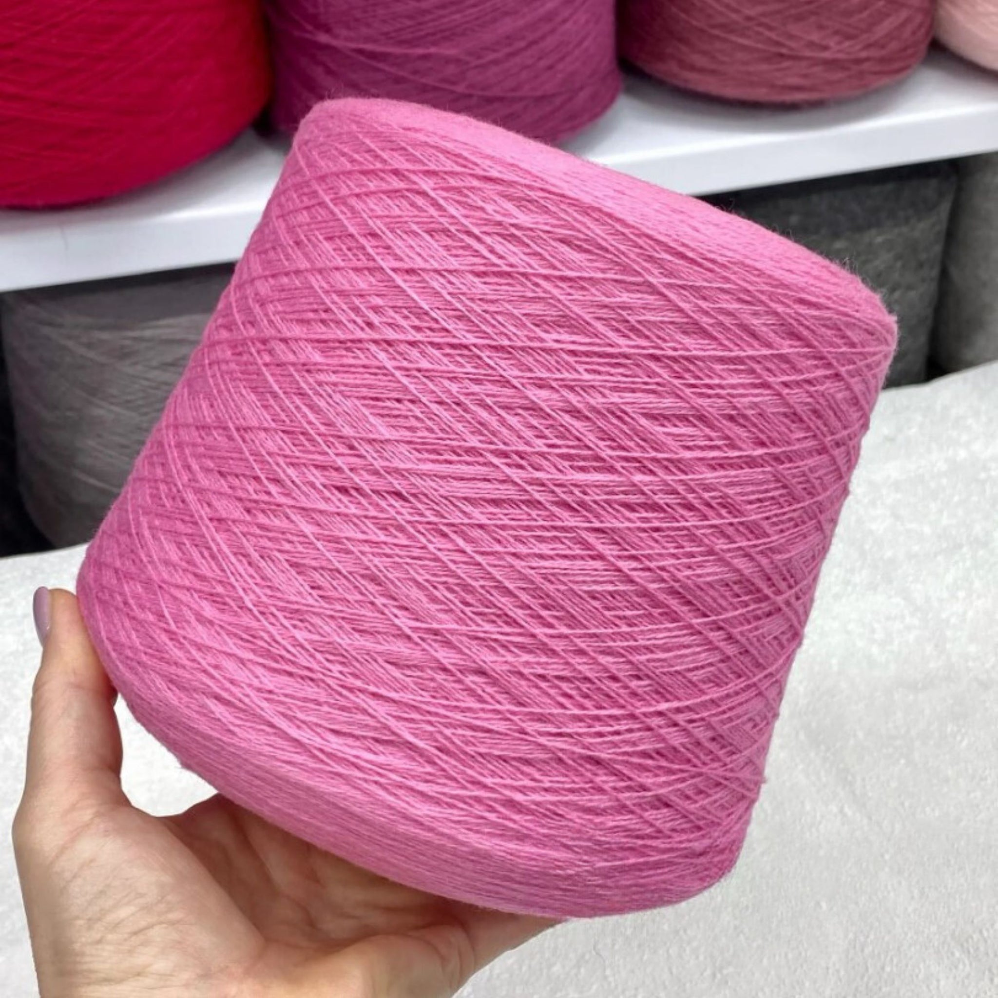 Hand holding a pink skein of merino yarn with more yarn in the background.