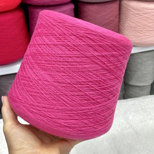 Hand holding a pink skein of merino yarn with more yarn spools in the background.
