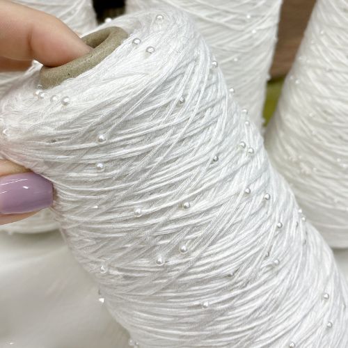 Close-up of white beaded cotton yarn with pearls on cone. 100% mercerized cotton with securely attached miniature iridescent beads — premium knitting yarn