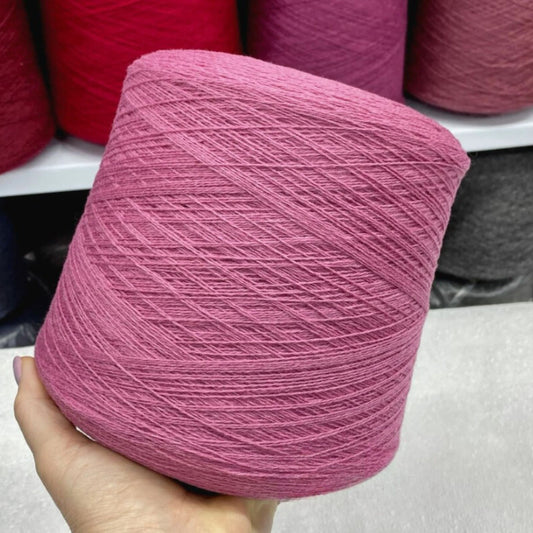 Pink yarn ball held in a hand with more yarn balls in the background