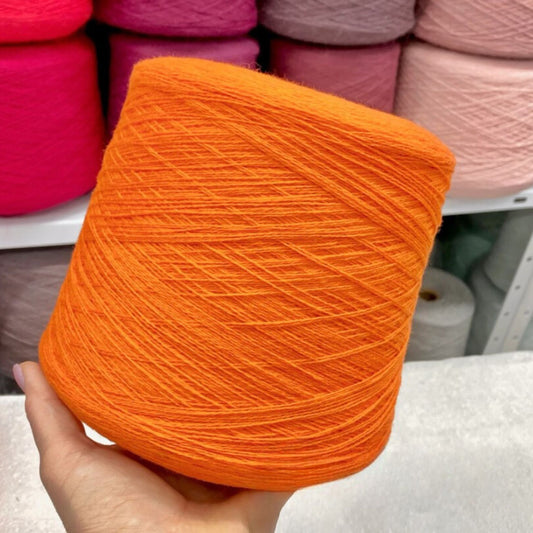 Orange yarn ball held in front of pink yarn balls on a shelf