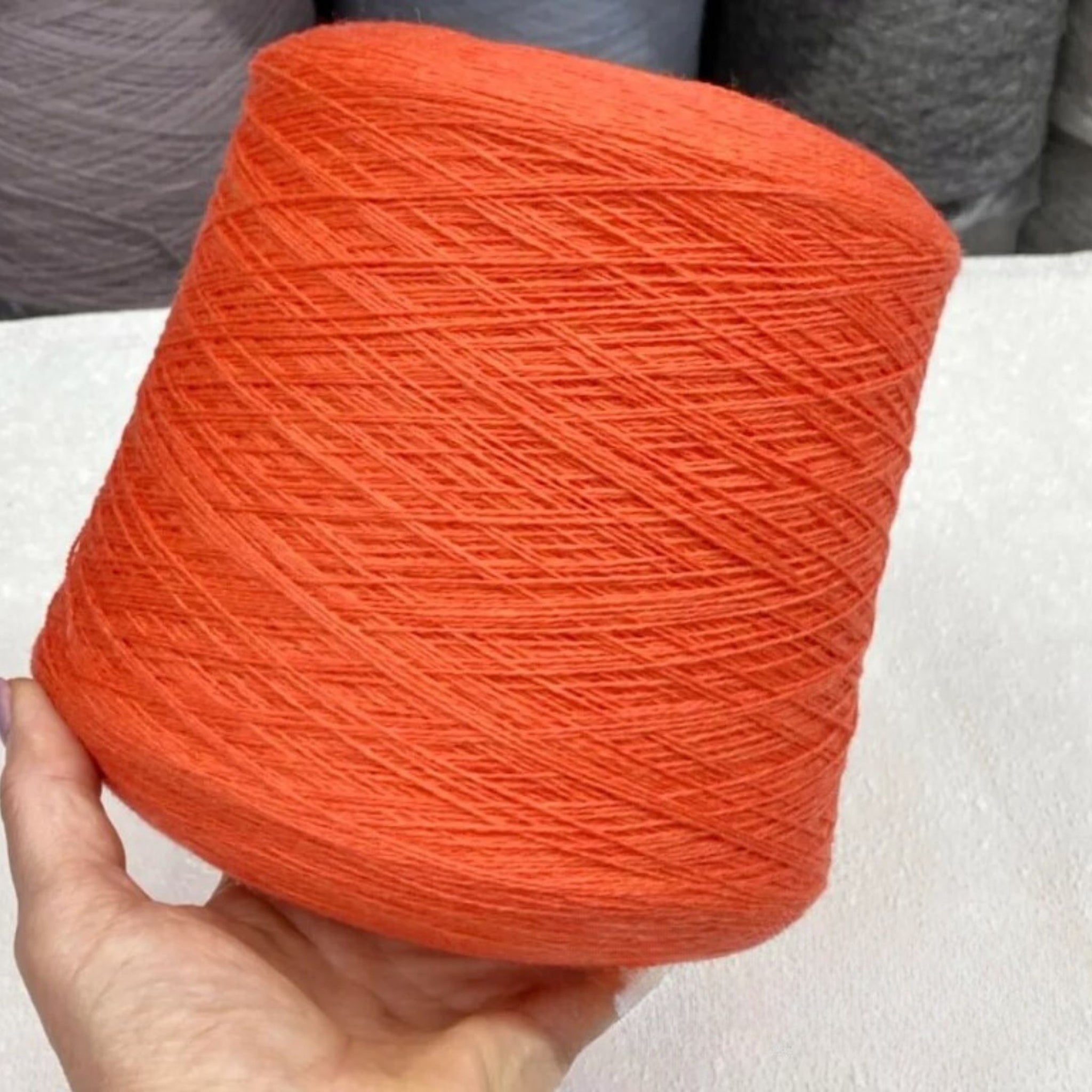 Orange yarn ball held by a hand on a neutral background