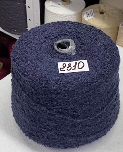 Blue spool of yarn with a label on a white surface, surrounded by more spools.Luxury fluffy Italian alpaca boucle captured in day