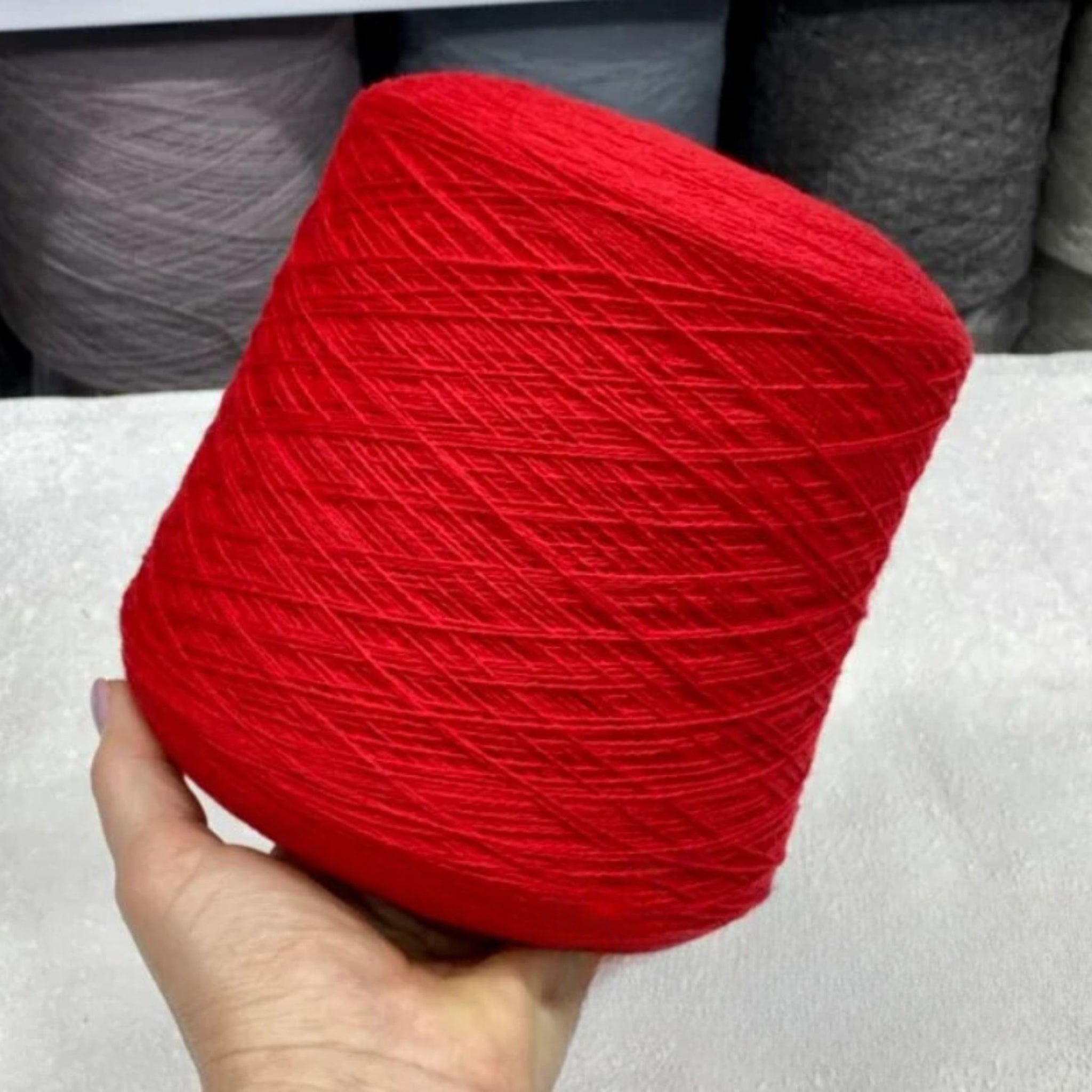 Red yarn ball held by a hand on a neutral background
