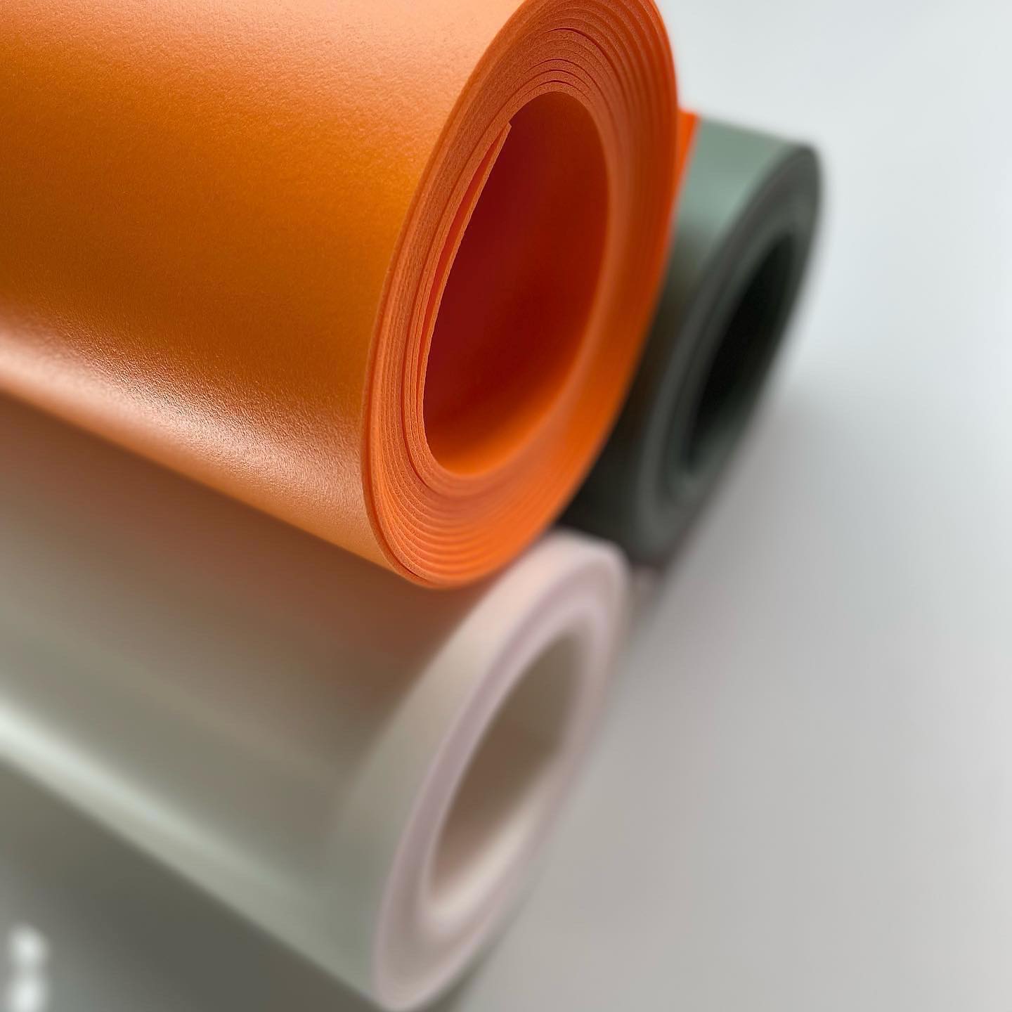 Close-up of orange, gray, and pink rolls of vinyl on a white background
