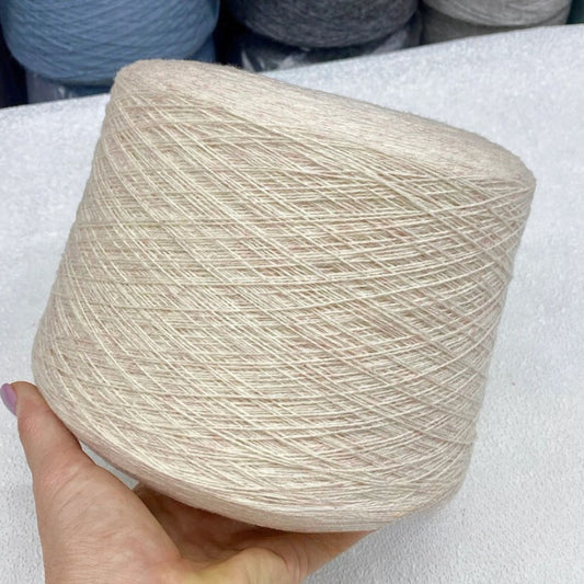 Spool of beige yarn held by a hand on a white surface with more yarn spools in the background.