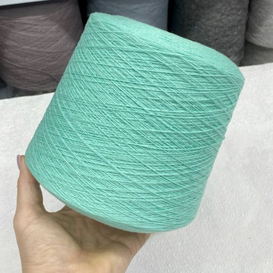 Turquoise yarn ball held by a hand with a neutral background