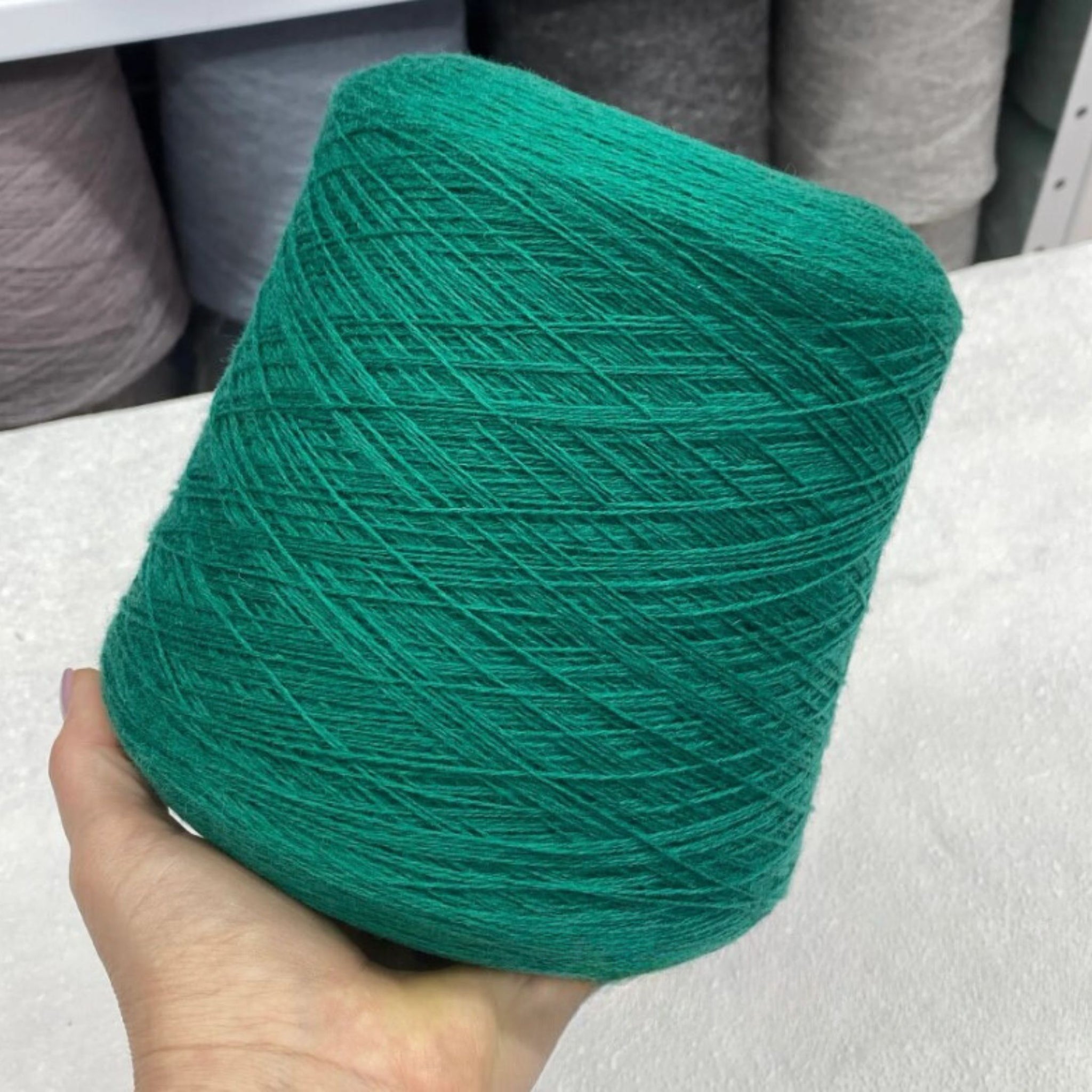 Green yarn ball held by a hand with more yarn balls in the background