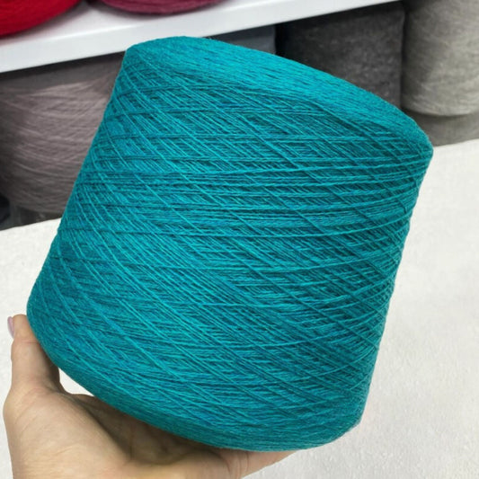 Turquoise yarn ball held in a hand with a blurred background