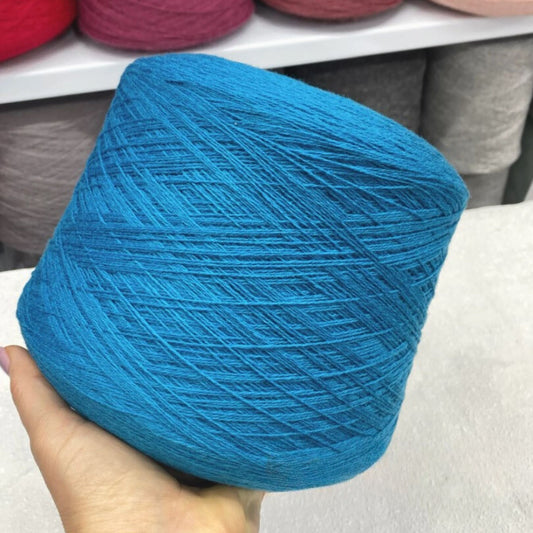 Blue yarn ball held by a hand with blurred yarn balls in the background