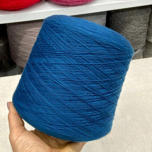 Blue yarn ball held by a hand on a light surface with blurred background