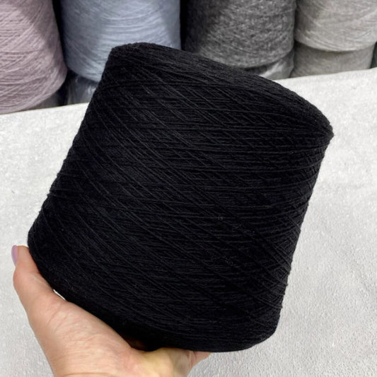 Black yarn ball held by a hand with gray yarn balls in the background