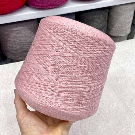 Pink yarn ball held in a hand with more yarn in the background