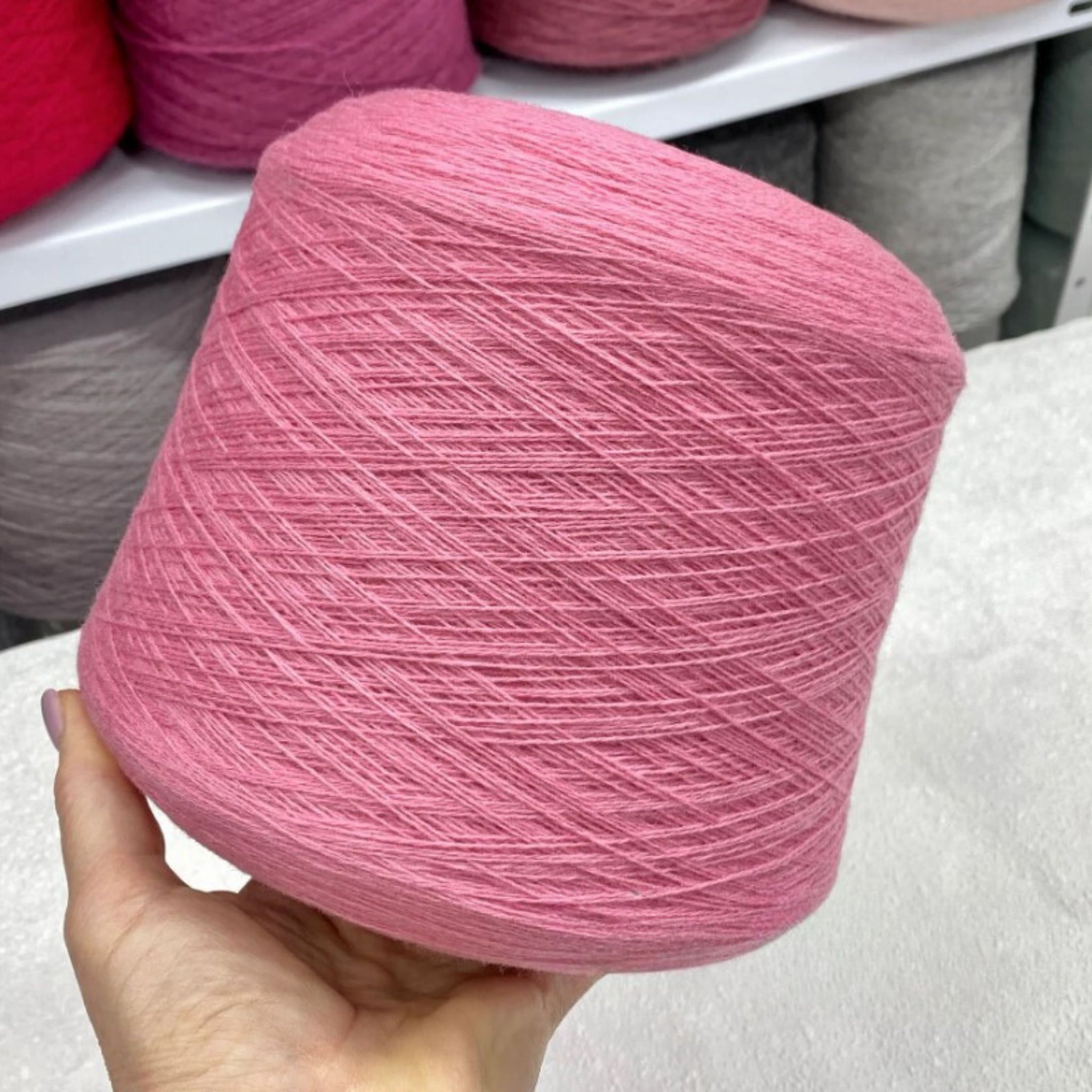 Pink yarn ball held by a hand with more yarn in the background