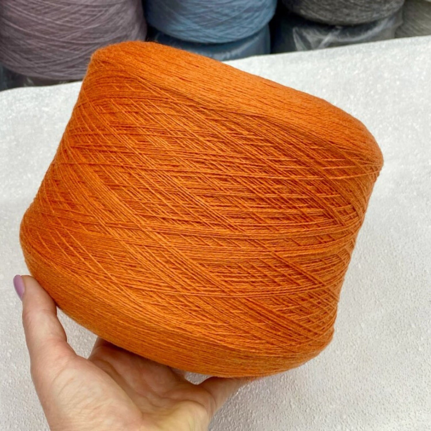 Orange yarn ball held by a hand with a neutral background