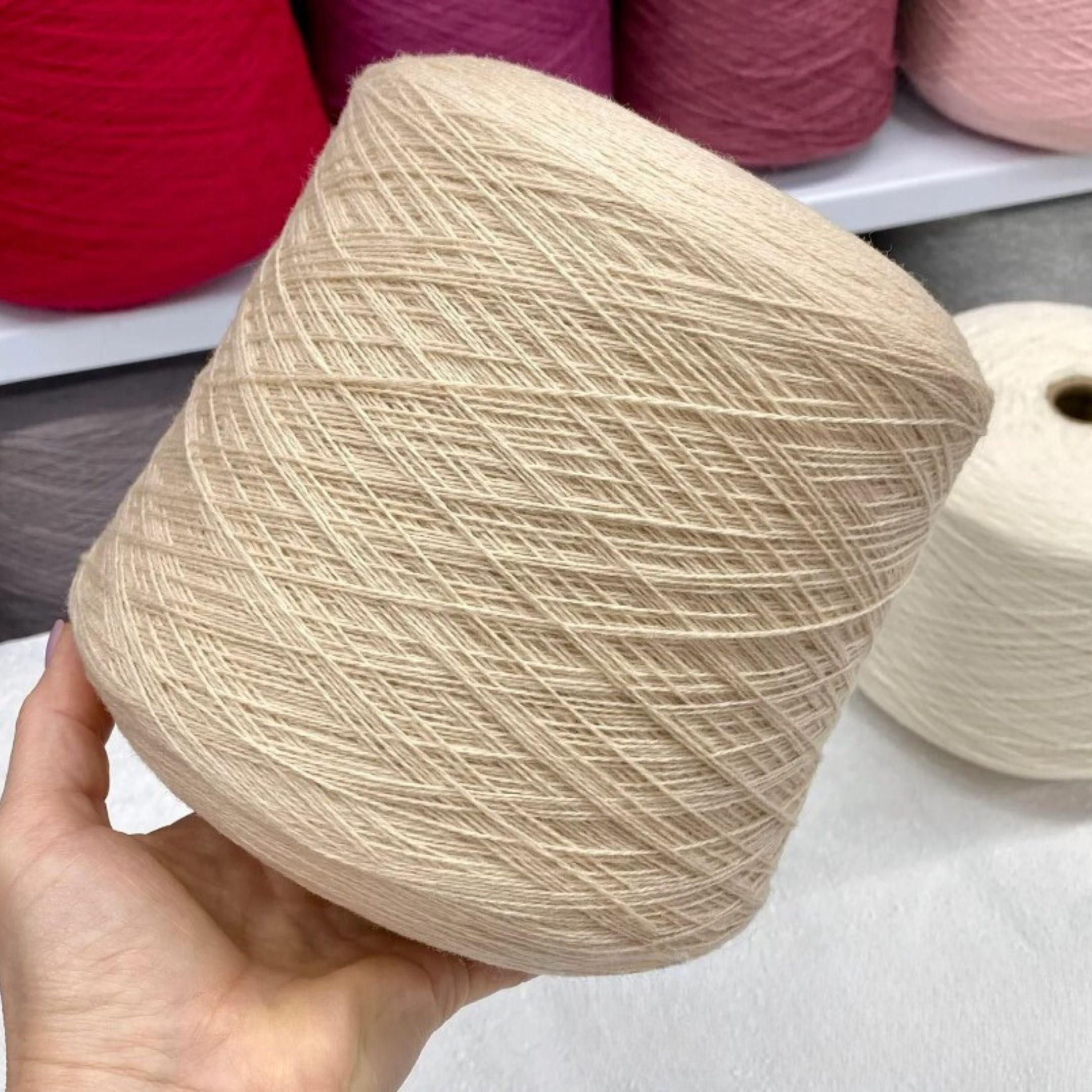 Beige yarn ball held in a hand with more yarn balls in the background