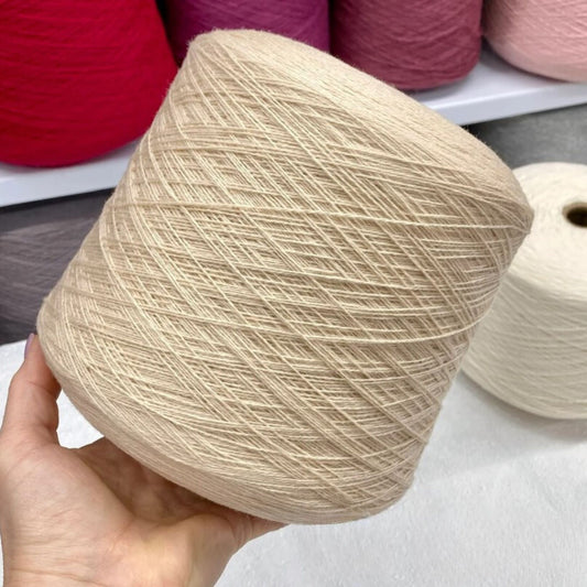 Beige yarn ball held in a hand with more yarn balls in the background