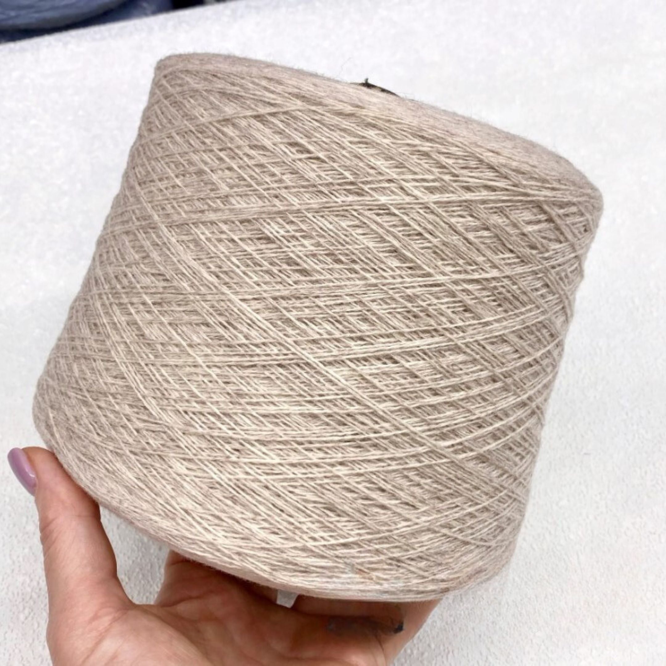 Beige yarn ball held by a hand on a white background