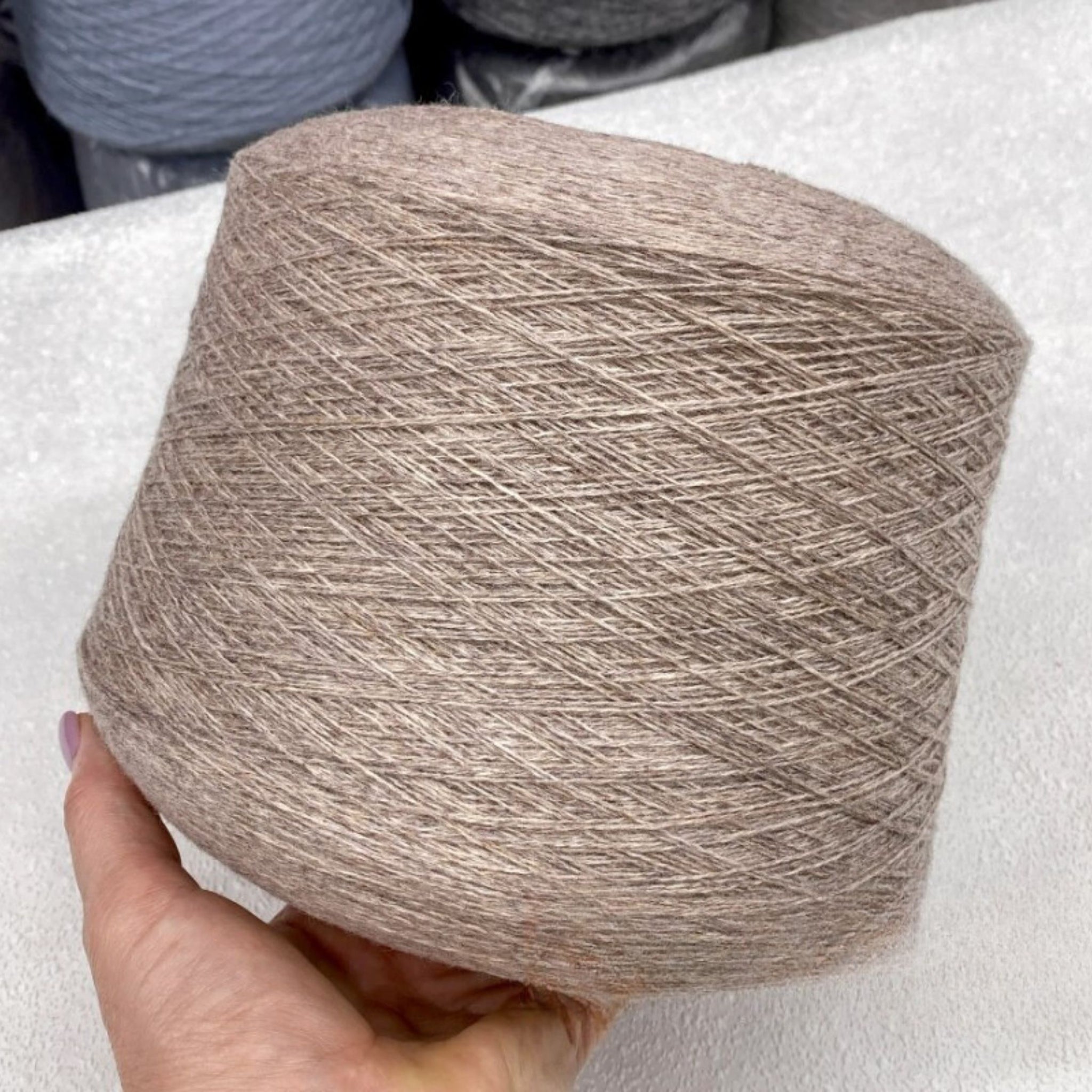 Hand holding a skein of brown yarn against a white background