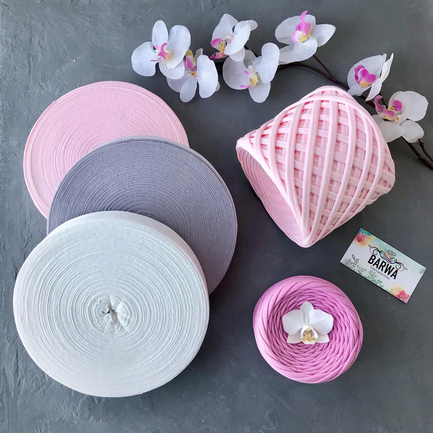 Stack of soft blush pink t-shirt yarn rolls 7-9mm, premium 100% virgin cotton chunky yarn styled with flowers and decorative pillow, perfect for crochet projects