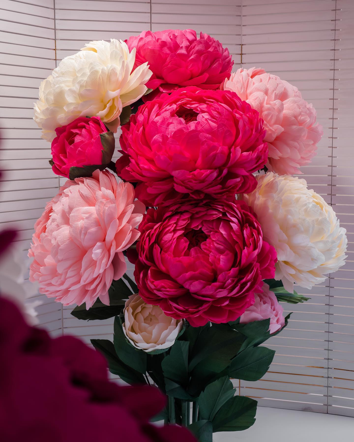 Giant paper peony flowers in vibrant hot pink, magenta and cream colors arranged in a beautiful bouquet against white blinds. Large handmade 65cm crepe paper peonies for wedding and home decor.