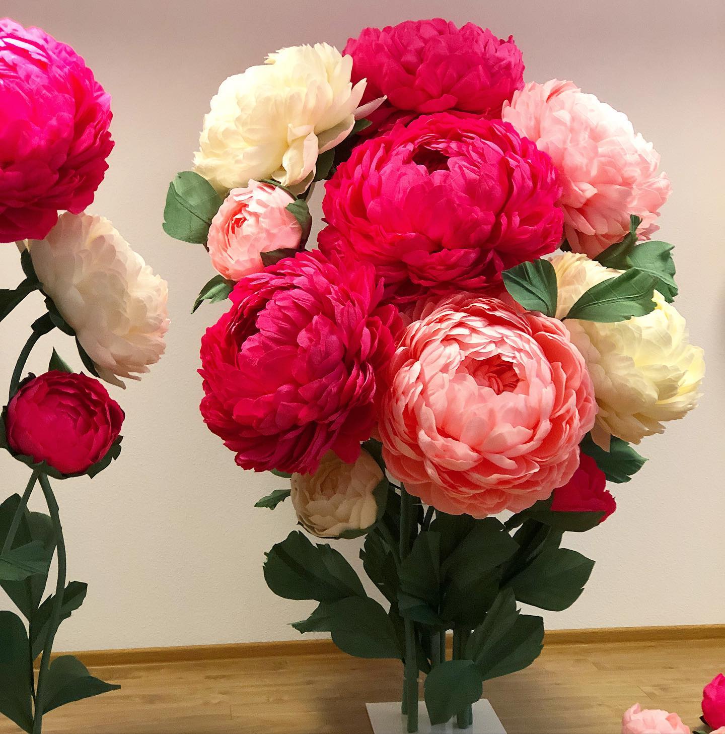 Vibrant bouquet of giant paper peony flowers in hot pink, coral, cream and white on a wooden floor. Beautiful handmade large peonies ideal for weddings, events and luxurious home décor.