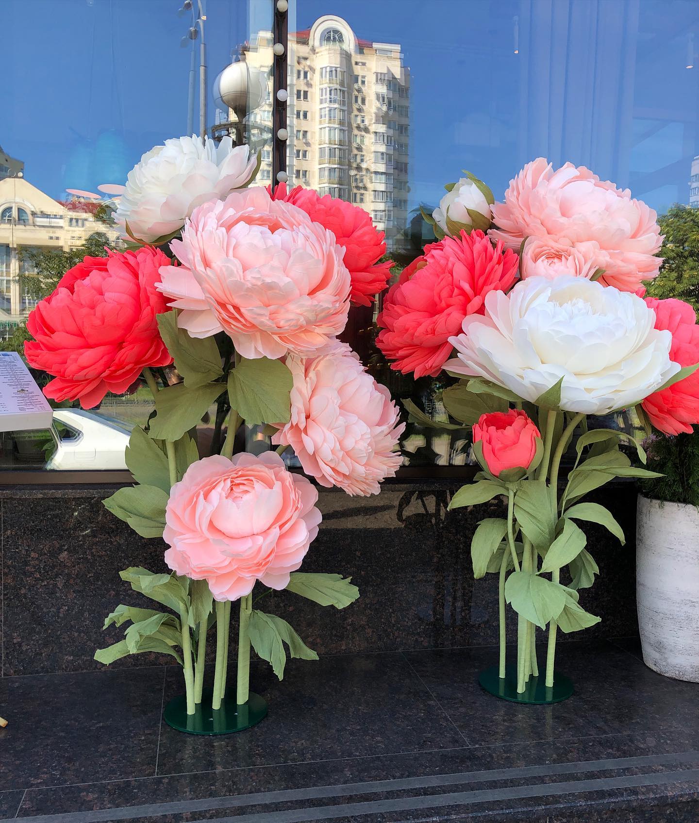 Vibrant giant paper peony flowers in bright pink, red and cream colors displayed in a modern hall with mirror wall. Large 65cm handmade crepe paper peonies creating a stunning wedding photo backdrop.